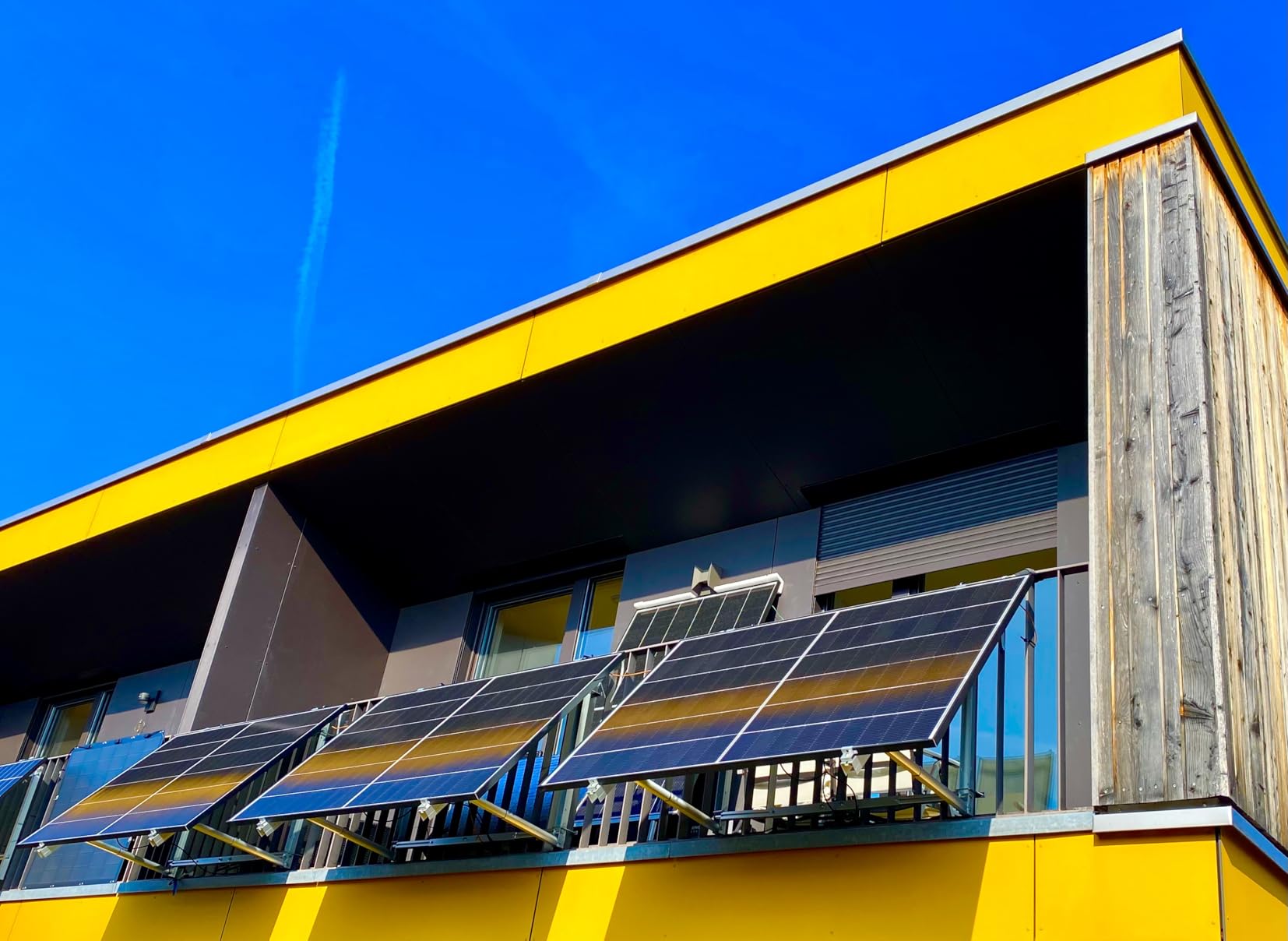 Vier angewinkelte Solarmodule an den Balkongeländern einer gelben Hausfassade vor blauem Himmel
