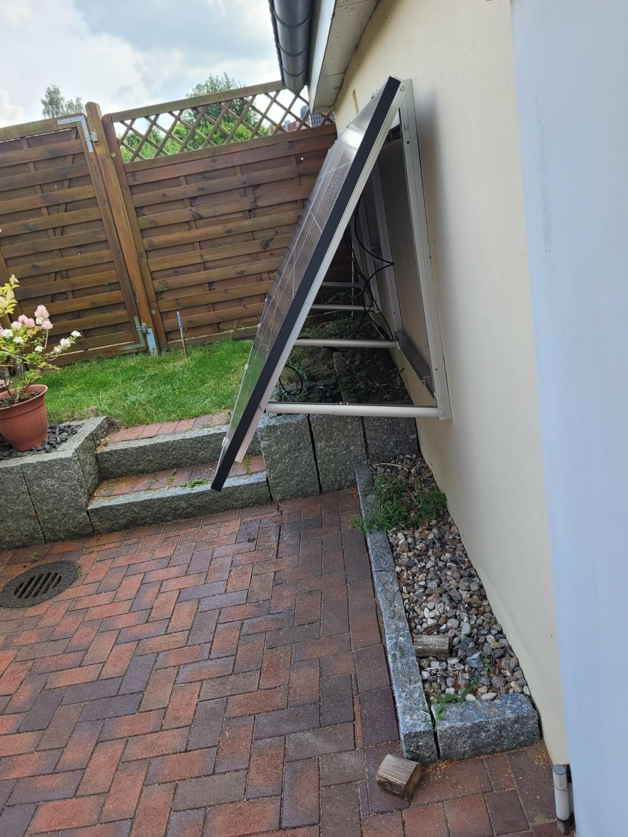 Solarmodul mit aufgeständerter Aluminium-Halterung an der Wand eines Gartenhauses, im Garten mit Holzzaun und Beeten montiert